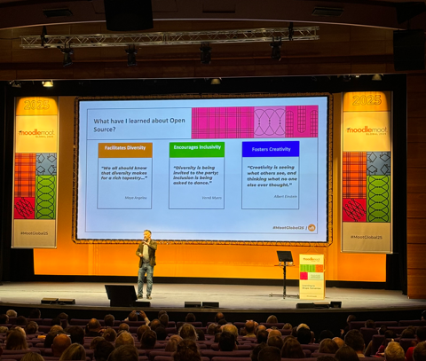 Attendees seated in an auditorium facing a brightly lit stage viewing a large presentation slide titled "What have I learned about OpenSource?" and highlights three points. 1. Facilitates Diversity 2. Encourages Inclusivity 3. Fosters Creativity. In front of the screen stood on the stage is Scott Anderberg, Moodle CEO.