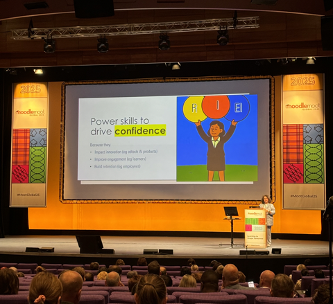A large auditorium with attendees sat in seated rows facing a brightly lit stage. On the stage is large screen which displays a slide titled "3 future-focused skills", listing: 1. Resilience Agility, 2. Inclusive Thinking, 3. Emotional Intelligence.