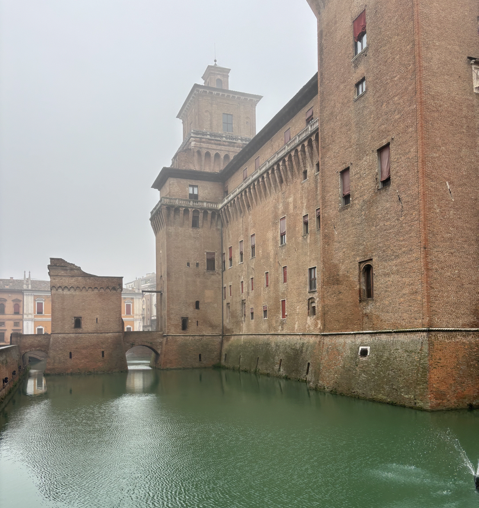 Moat and brick walls of Castello Estense in Ferrara on an overcast day.