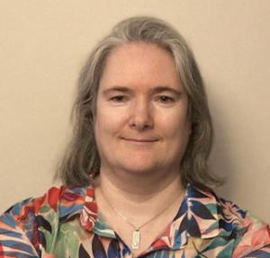 A woman withshoulder-length grey hair, and wearing a colourful patterned blouse smiles.