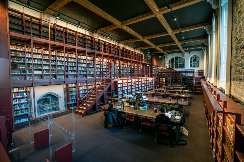 Woodlock Hall Library on DCU's All Hallows Campus, with tall bookshelves, exposed timber ceiling beams, and students studying at desks.